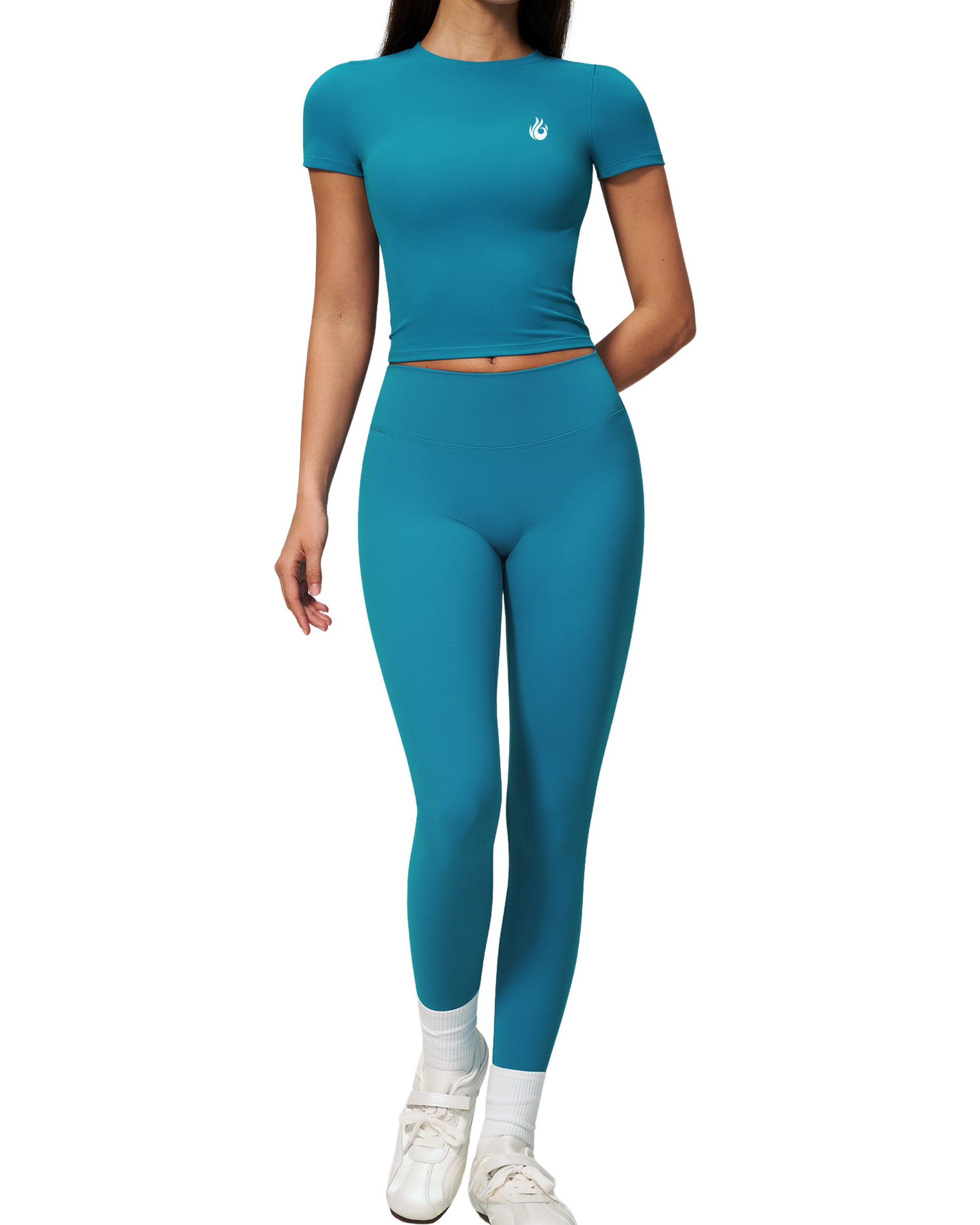 A model wearing a matching teal short-sleeve crop top and high-waisted leggings set, styled with white socks and white sneakers, against a plain white background.