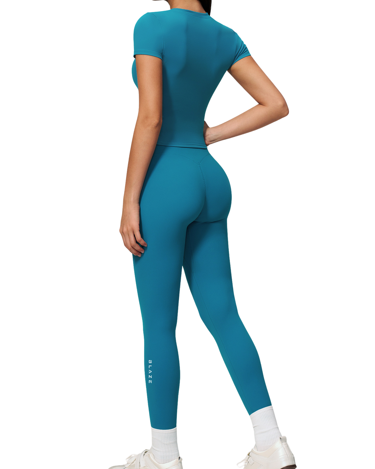 A model shown from the back wearing a teal short-sleeve athletic bodysuit and matching leggings, paired with white socks and white sneakers, against a solid white background.